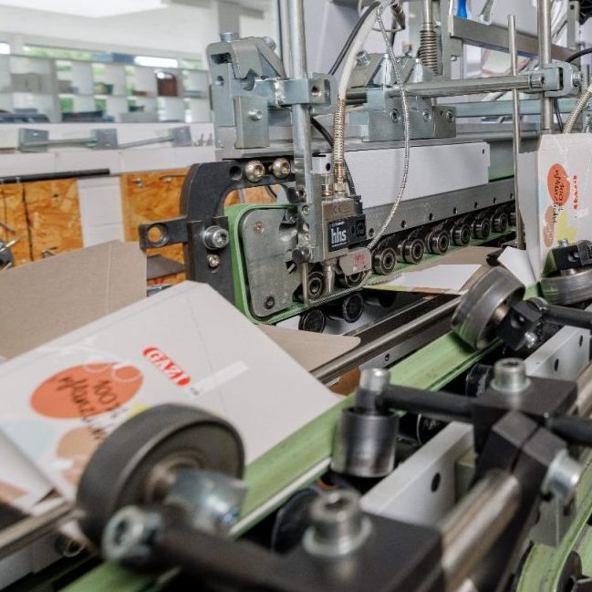 Verpackung läuft durch eine Falz- und Klebestraße für die Fertigstellung